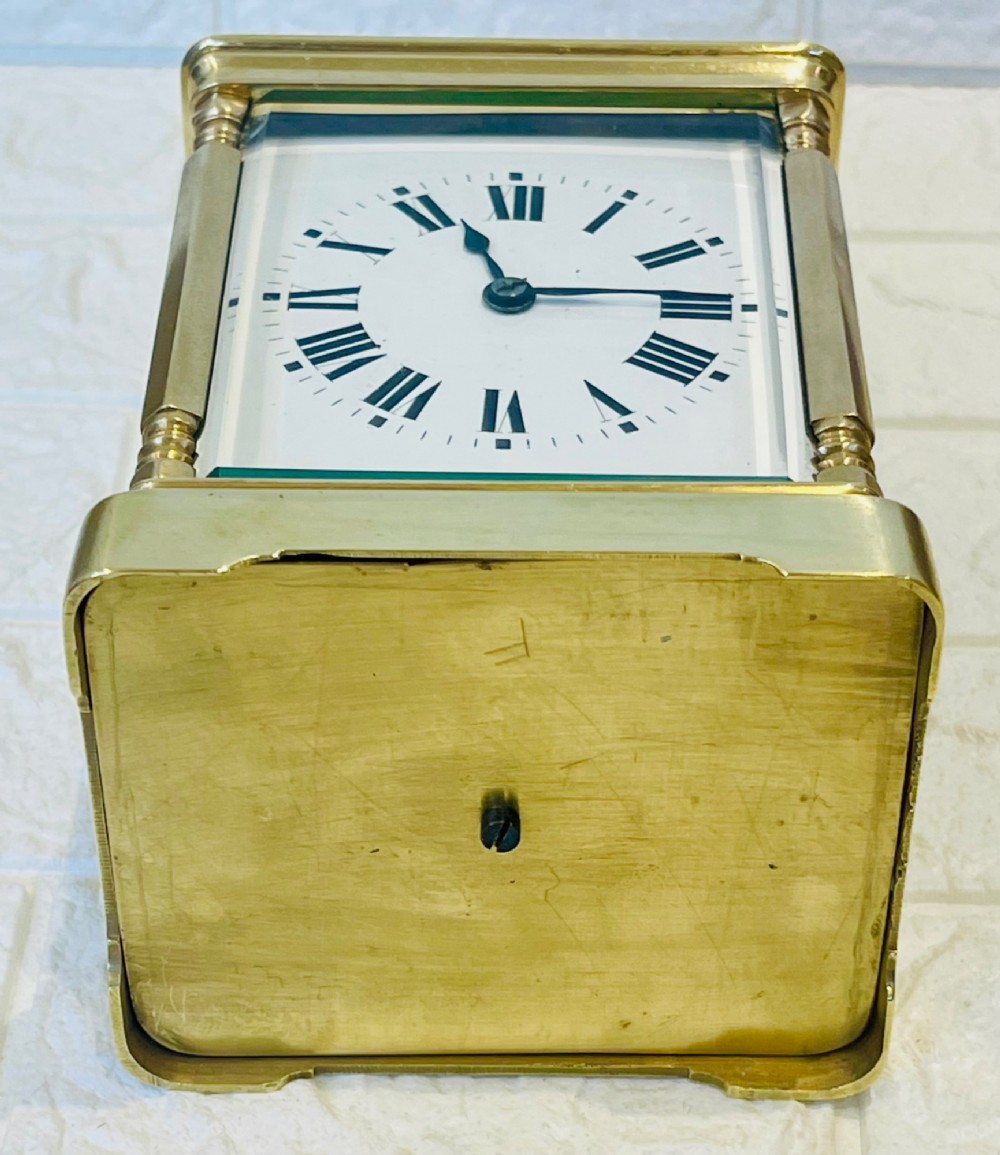 A rectangular brass carriage clock featuring a hinged carrying handle, bevelled glass panels, a top repeat button, and a white enamel dial with black Roman numerals. View XI