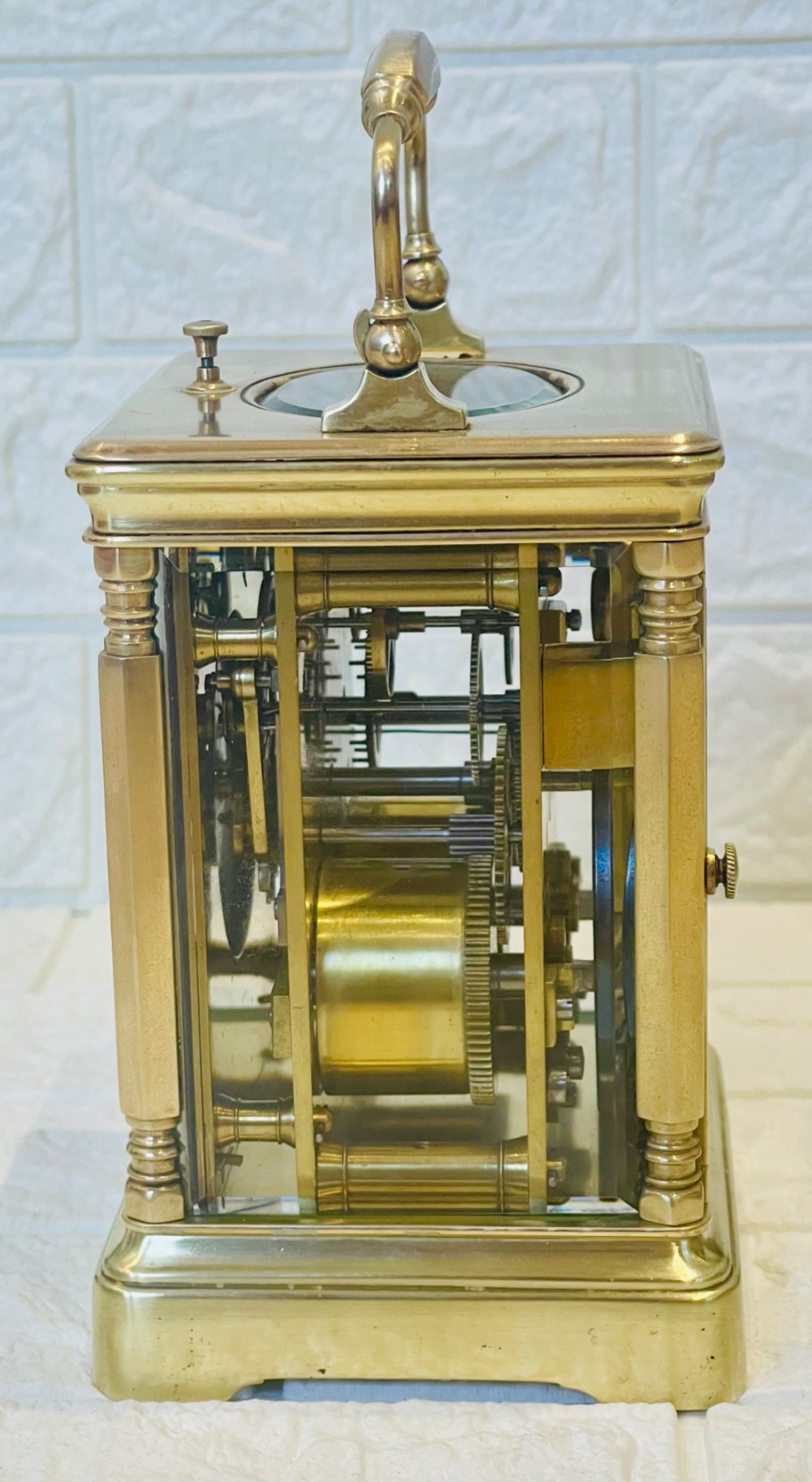 A rectangular brass carriage clock featuring a hinged carrying handle, bevelled glass panels, a top repeat button, and a white enamel dial with black Roman numerals. View XII