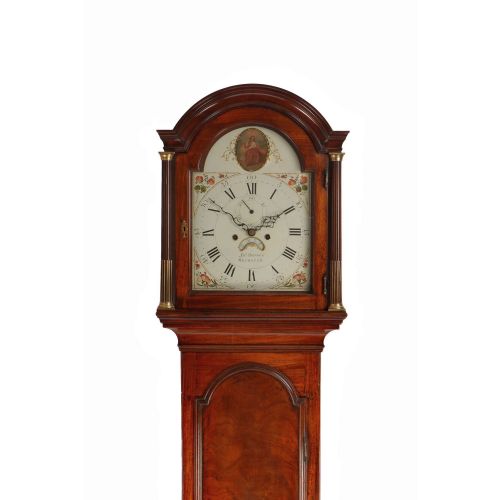 fig 1. A Georgian mahogany longcase clock featuring an arched hood with brass fluted columns, a painted dial with Roman numerals, and a flame mahogany trunk door.