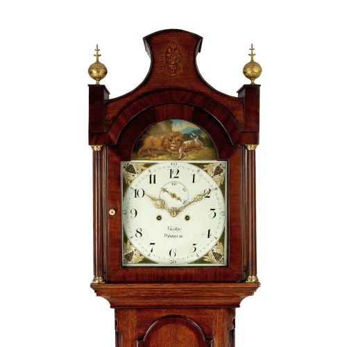 fig 1. An antique wooden longcase clock featuring a painted dial with an automata scene, topped with brass finials and an arched hood.