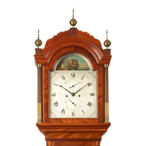fig 1. A tall Georgian flame mahogany longcase clock featuring brass finials and a painted arch dial displaying a rocking ship automaton.