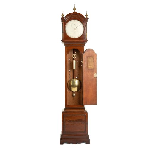 fig 2. An antique mahogany longcase regulator clock with three brass finials on an arched hood, a white regulator dial, and a flame mahogany trunk door.