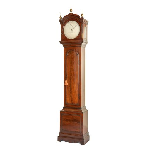 fig 3. An antique mahogany longcase regulator clock with three brass finials on an arched hood, a white regulator dial, and a flame mahogany trunk door.
