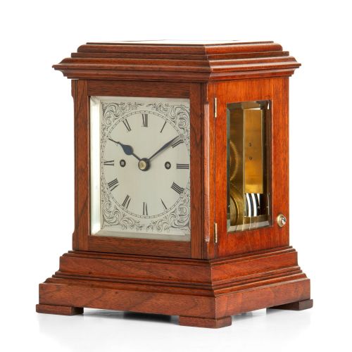 fig 1. An antique walnut five-glass mantel clock featuring a stepped wooden base, glass panels, and a silvered dial with Roman numerals.