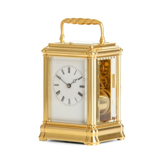 fig 1. A French brass carriage clock featuring a rectangular bevelled glass case, a folding top handle, and a white enamel dial with black Roman numerals.
