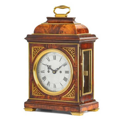 fig 2. A Georgian mahogany table clock featuring an arched bell top with a brass carrying handle, gilt brass spandrels, and a circular silvered dial with Roman numerals.