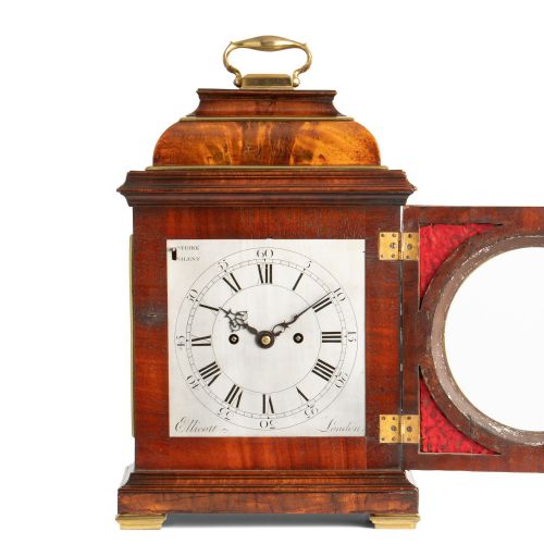 fig 1. A Georgian mahogany table clock featuring an arched bell top with a brass carrying handle, gilt brass spandrels, and a circular silvered dial with Roman numerals.