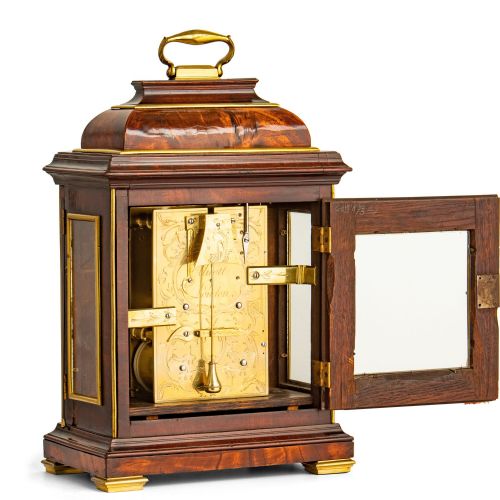 fig 3. A Georgian mahogany table clock featuring an arched bell top with a brass carrying handle, gilt brass spandrels, and a circular silvered dial with Roman numerals.