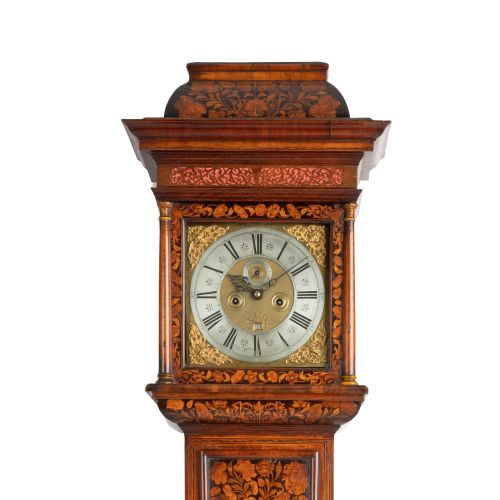 fig 3. An antique walnut longcase clock featuring floral marquetry inlays, a square brass dial with a silvered chapter ring, and a glass lenticle set into the trunk door.