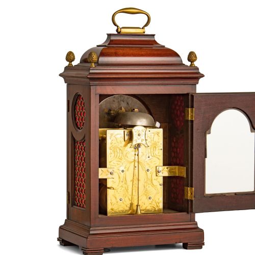 fig 2. A Georgian mahogany striking table clock featuring an arched brass and silvered dial, decorative corner spandrels, a bell top with brass handle, and pineapple finials.