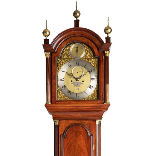 fig 1. A Georgian flame mahogany longcase clock featuring an arched hood with three brass finials and an engraved brass dial.