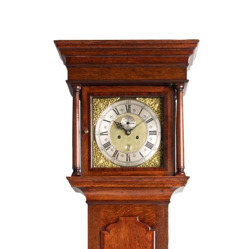 fig 1. An antique Georgian oak longcase clock featuring a square brass dial with Roman numerals and turned hood columns.