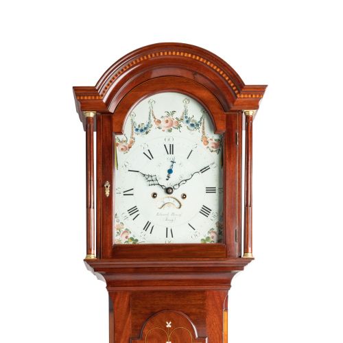 fig 1. An antique mahogany Channel Island longcase clock featuring a painted arched dial with floral detail, an inlaid waist door, and turned hood columns.