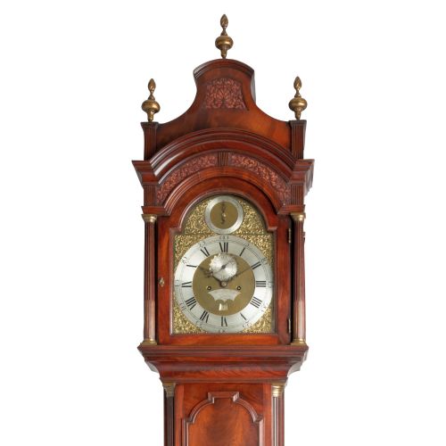 fig 1. A Georgian flame mahogany longcase clock featuring an arched brass dial with brass finials on a shaped hood.