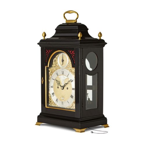 fig 1. An 18th-century style ebonised bracket clock featuring a bell top case with a brass handle, pinecone finials, and a silvered brass dial with decorative spandrels.