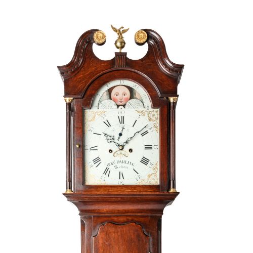 fig 2. A tall dark oak longcase clock featuring a swan-neck pediment, brass eagle finial, arched painted dial with moonphase movement, and a central trunk door.