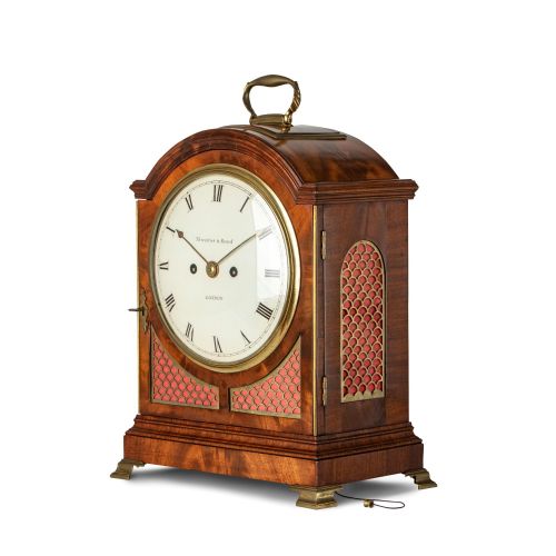 fig 1. An arched Regency mahogany bracket clock featuring a circular dial signed Thwaites and Reed London, framed by a brass bezel and brass fish-scale fretwork with red backing.