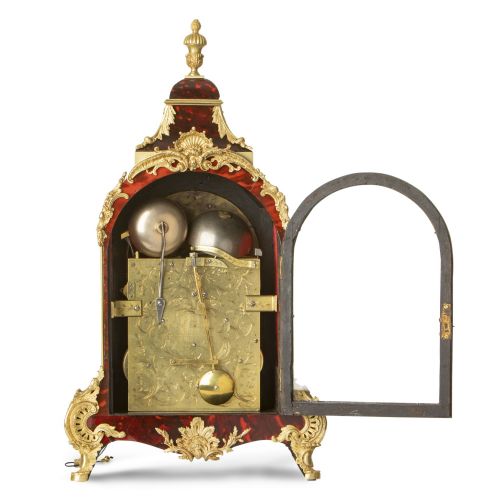 fig 2. An arched red tortoiseshell bracket clock adorned with gilded ormolu mounts, Rococo scroll feet, and a silvered dial.