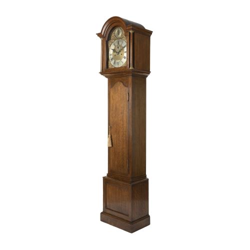 fig 1. A compact oak longcase clock featuring an arched hood, brass dial with Roman numerals, and a waist door with a hanging tassel.