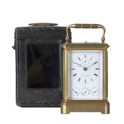 fig 1. A rectangular brass carriage clock featuring a top carrying handle, glass panels, a main white enamel dial with Roman numerals, and three subsidiary dials for calendar functions.
