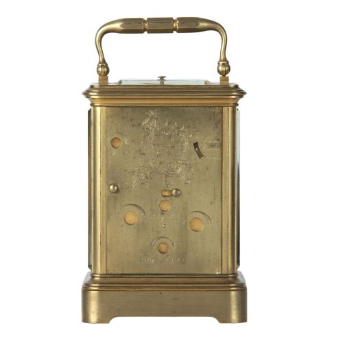 fig 2. A rectangular brass carriage clock featuring a top carrying handle, glass panels, a main white enamel dial with Roman numerals, and three subsidiary dials for calendar functions.