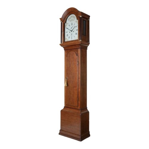 fig 1. An antique oak longcase clock featuring a rounded arched hood, a white painted dial with Roman numerals, and a tall slender trunk set on a plinth base.