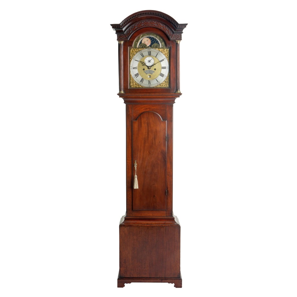An antique Georgian mahogany longcase clock featuring an arched hood with fluted columns and a brass dial with an integrated moonphase display.