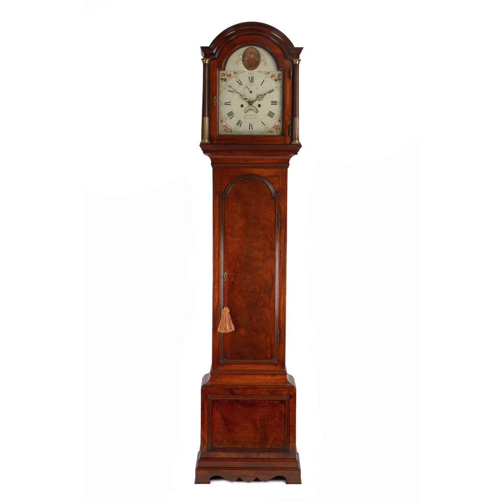 A Georgian mahogany longcase clock featuring an arched hood with brass fluted columns, a painted dial with Roman numerals, and a flame mahogany trunk door.
