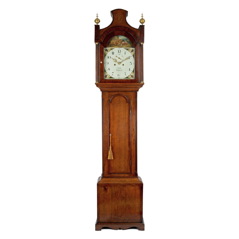 An antique wooden longcase clock featuring a painted dial with an automata scene, topped with brass finials and an arched hood.