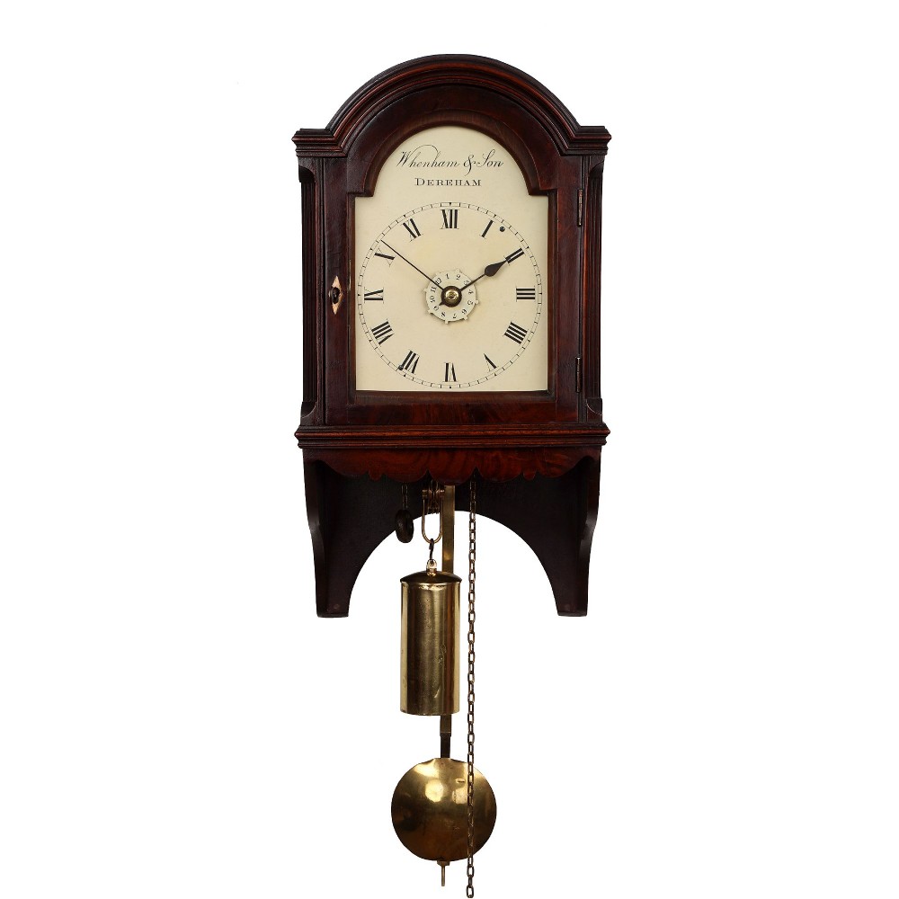 An antique dark mahogany hooded wall clock featuring an arched top, cream painted dial signed Wenham & Son Dereham, visible brass pendulum, and brass weight.
