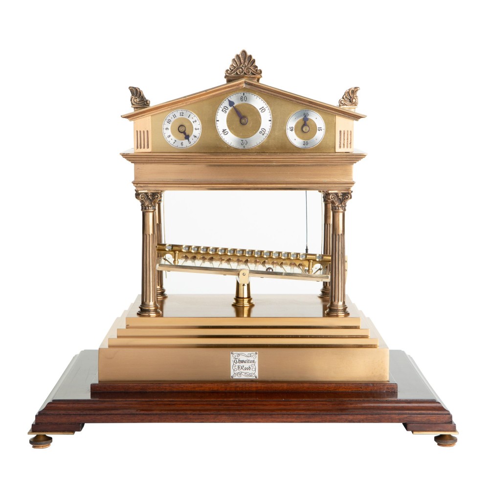 A brass Congreve rolling ball clock with classical pediment top and columns mounted on a dark wood base.
