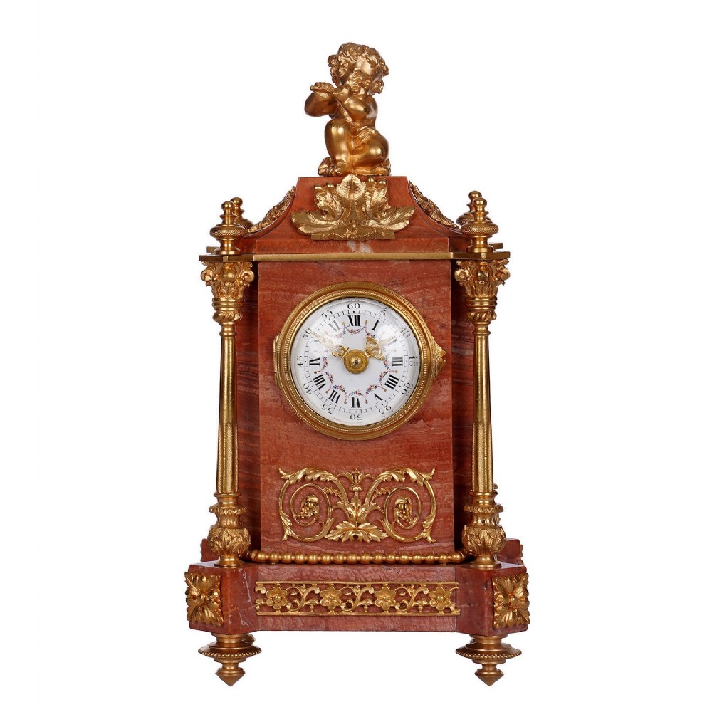 A French pink marble and ormolu mantel clock featuring a gilt bronze figure of a flute-playing cherub on top, classical columns, and a white enamel dial with floral detailing.