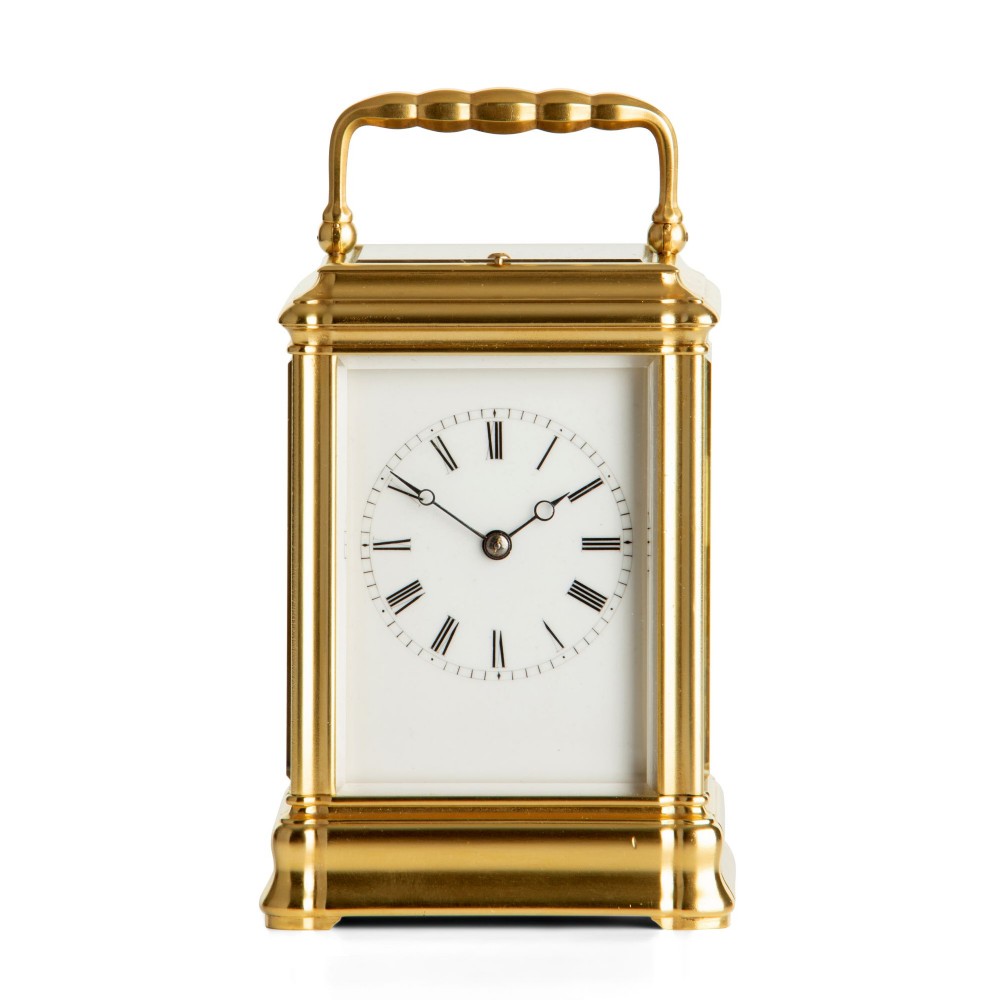 A French brass carriage clock featuring a rectangular bevelled glass case, a folding top handle, and a white enamel dial with black Roman numerals.