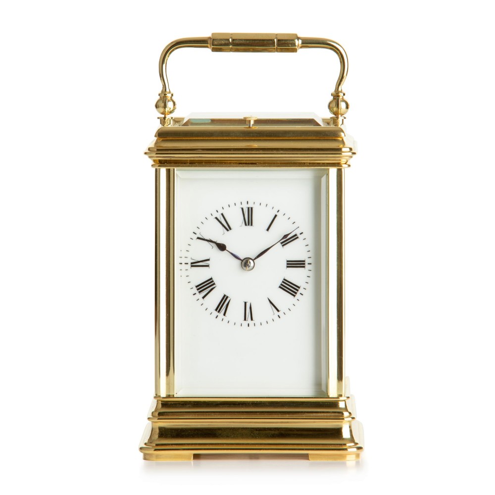 A rectangular polished brass French carriage clock featuring a top carrying handle, bevelled glass side panels, and a white enamel dial with Roman numerals.