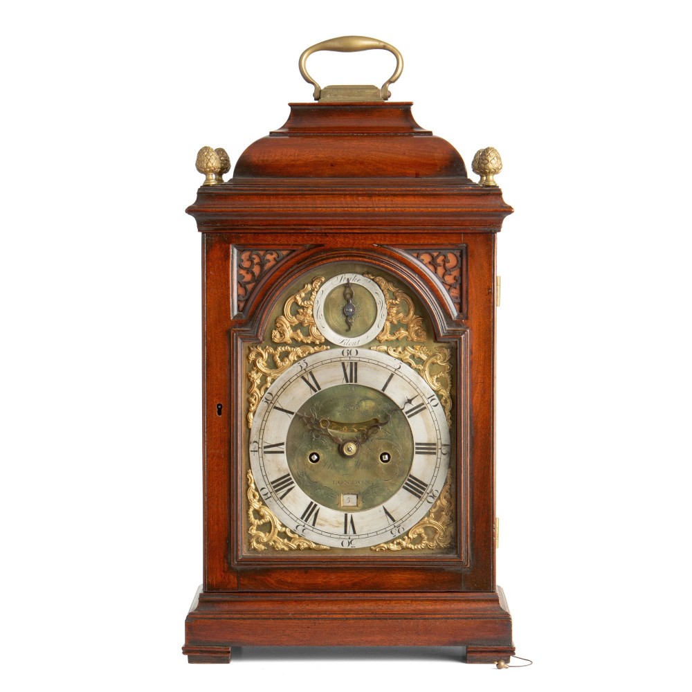 A Georgian mahogany striking table clock featuring an arched brass and silvered dial, decorative corner spandrels, a bell top with brass handle, and pineapple finials.