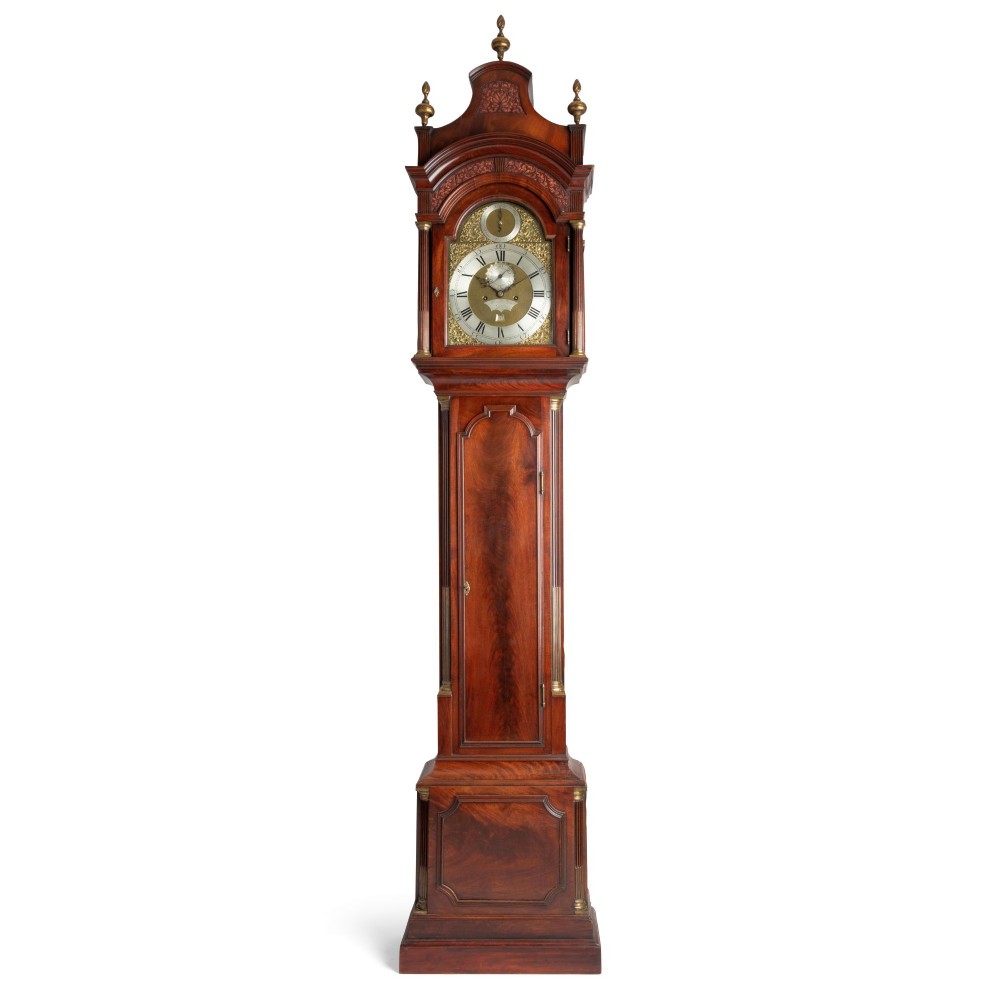 A Georgian flame mahogany longcase clock featuring an arched brass dial with brass finials on a shaped hood.