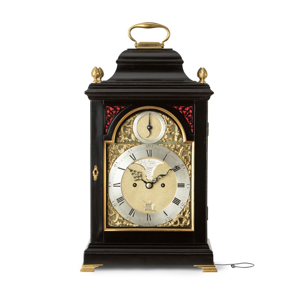 An 18th-century style ebonised bracket clock featuring a bell top case with a brass handle, pinecone finials, and a silvered brass dial with decorative spandrels.