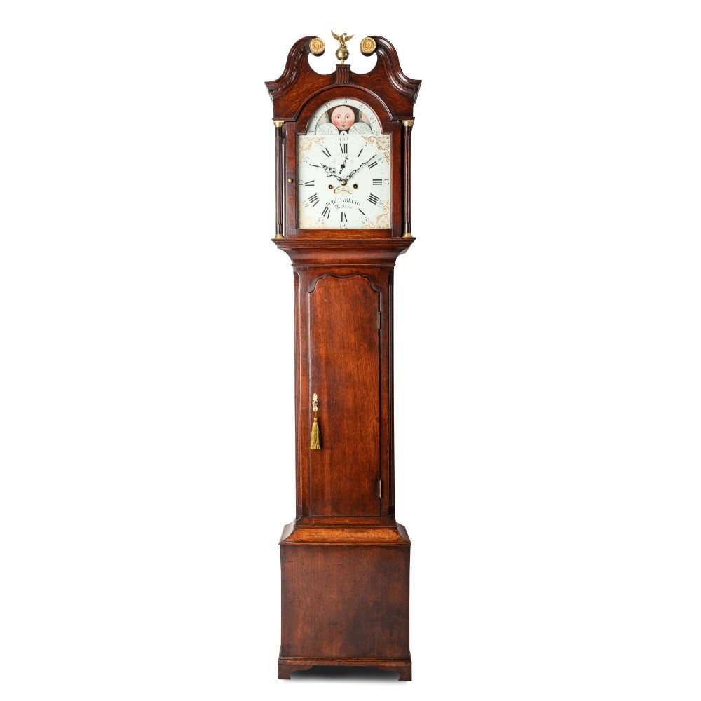 A tall dark oak longcase clock featuring a swan-neck pediment, brass eagle finial, arched painted dial with moonphase movement, and a central trunk door.