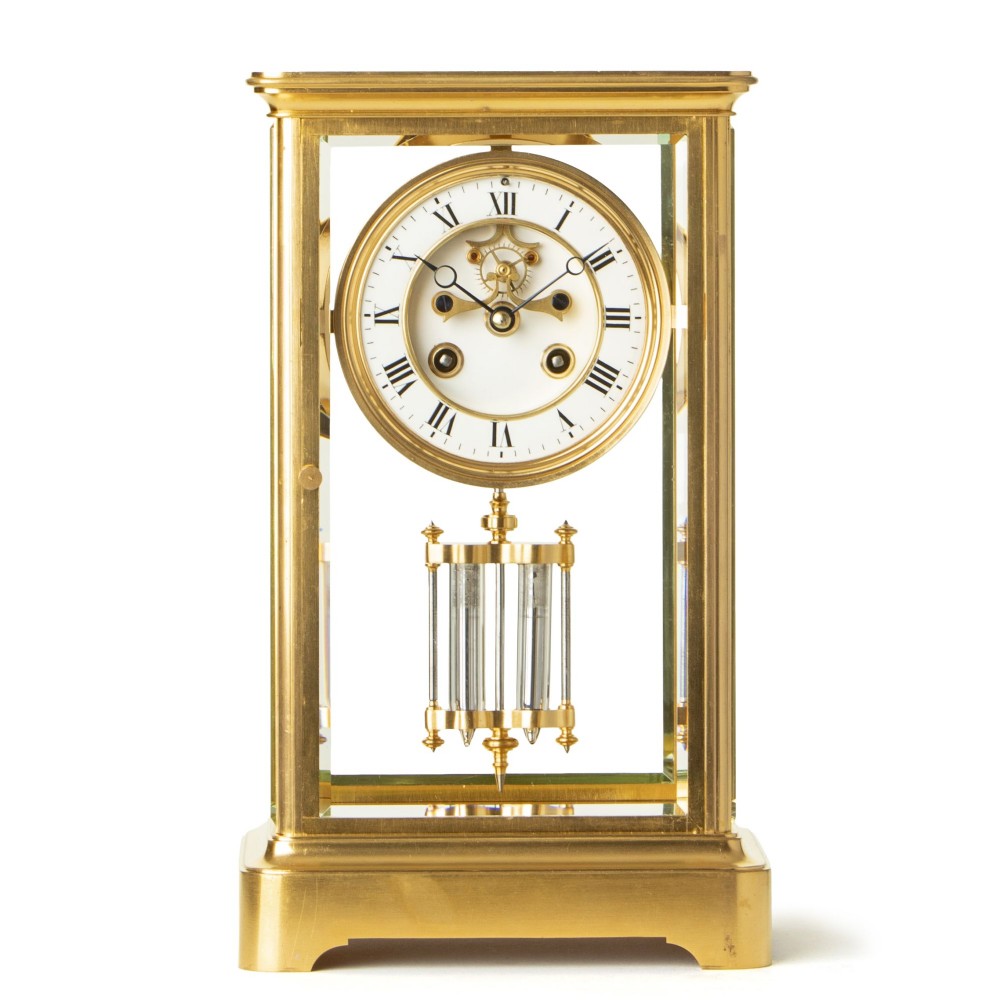 A rectangular brass and bevelled glass French four-glass clock featuring a white enamel dial with Roman numerals and a visible pendulum.