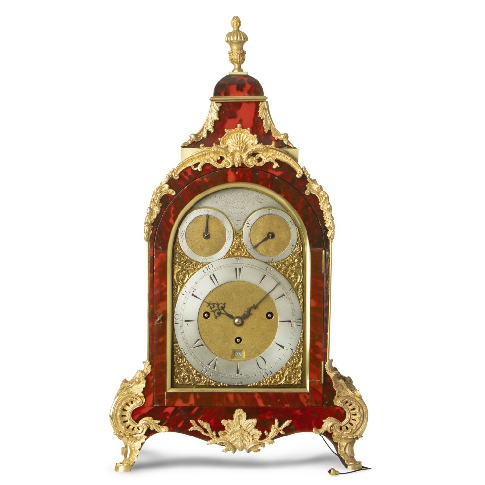 An arched red tortoiseshell bracket clock adorned with gilded ormolu mounts, Rococo scroll feet, and a silvered dial.