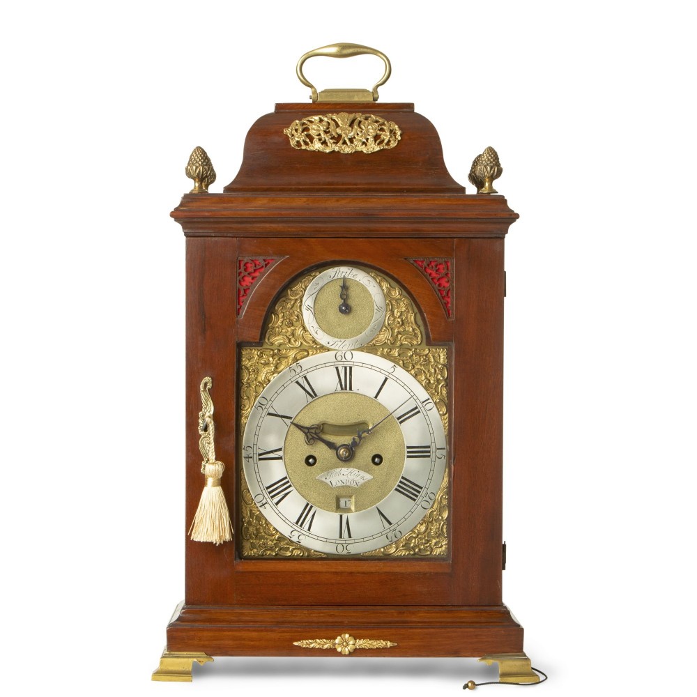 A Georgian mahogany bracket clock with a brass carrying handle, pinecone finials, and an arched brass dial signed Robert Higgs London.