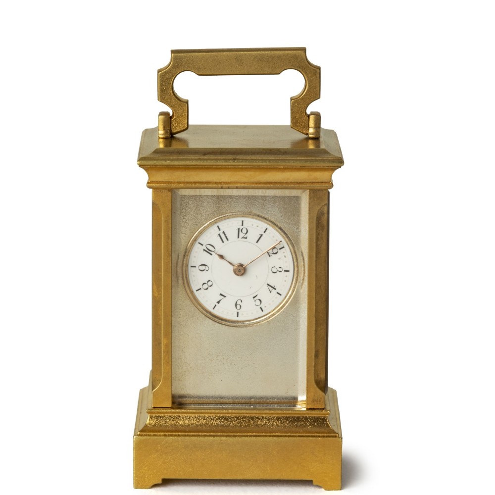 A subminiature gilt brass carriage clock featuring a top carrying handle, glass side panels, and a white enamel dial with Arabic numerals.