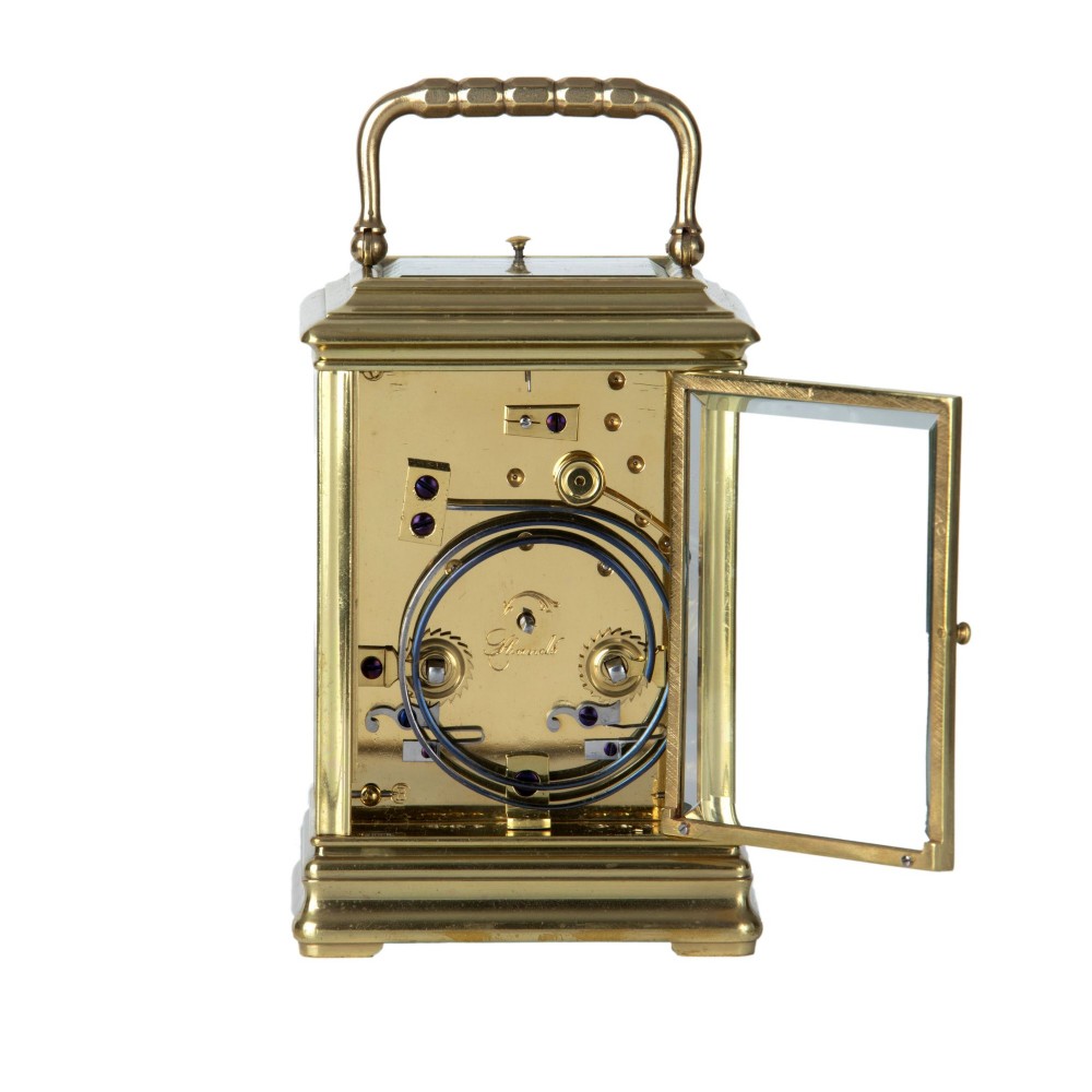 A solid brass repeating carriage clock viewed from behind with its bevelled glass rear door open to reveal the mechanical movement and coiled gong.