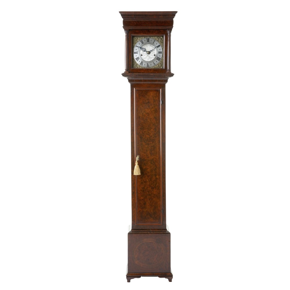 A miniature longcase clock crafted from figurative walnut veneer featuring a brass dial with Roman numerals and a plinth base.