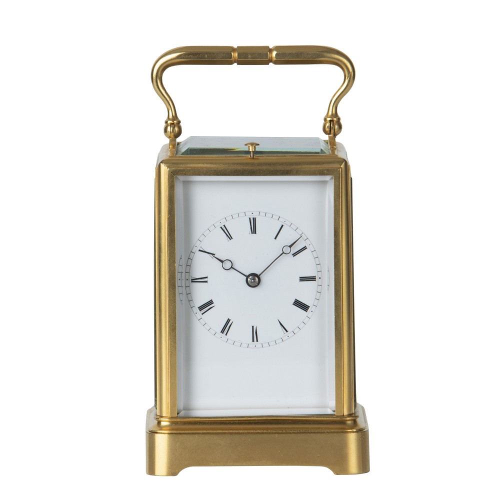 A rectangular brass repeating carriage clock featuring a top carrying handle, glass side panels, and a white enamel dial with black Roman numerals.