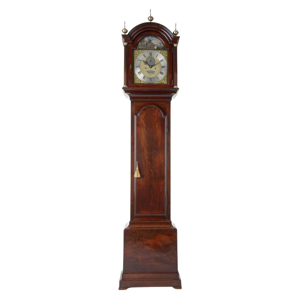 A Georgian flame mahogany longcase clock with brass urn finials and an arched brass dial depicting a moving windmill automata scene.