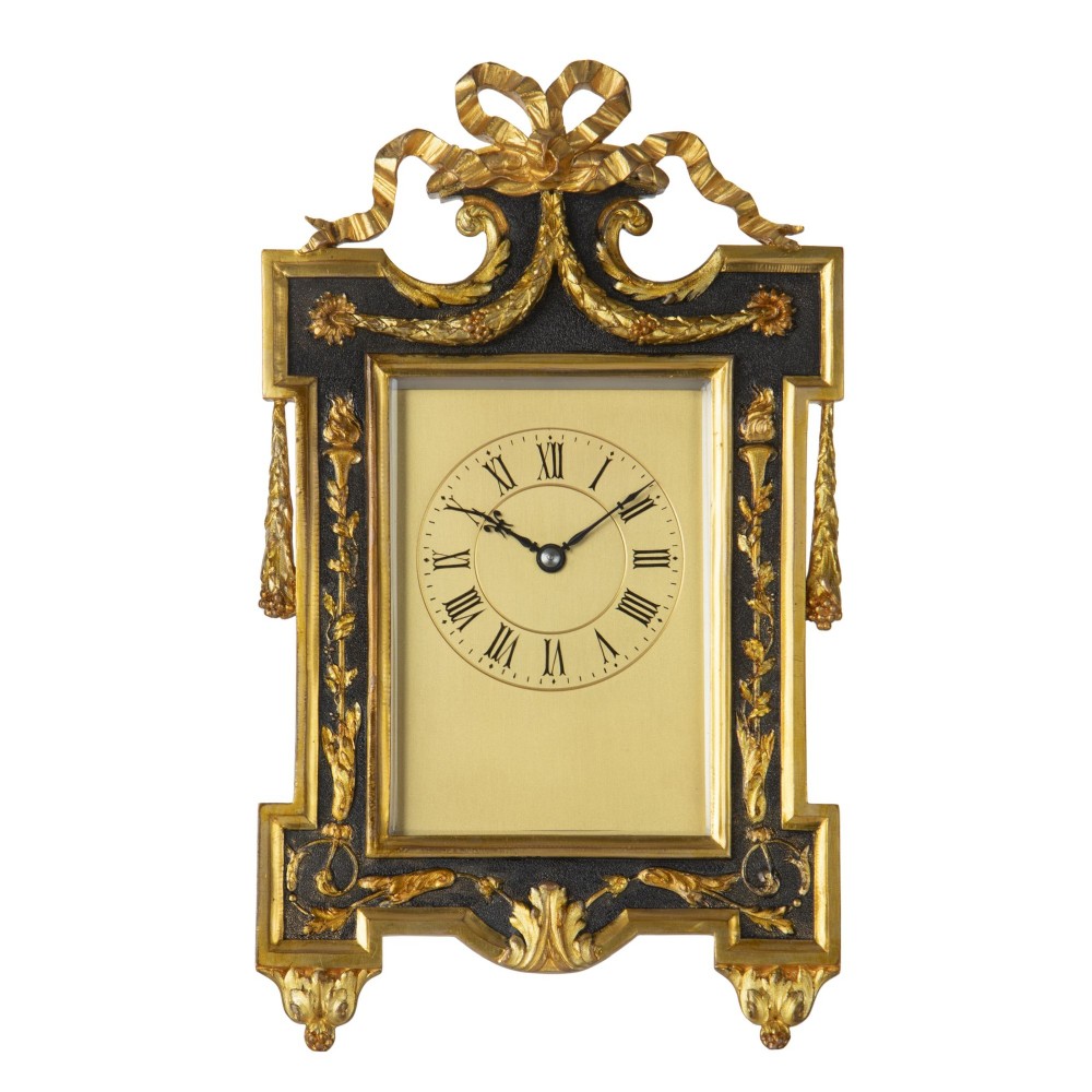 An ornate rectangular gilt brass strut clock featuring ribbon bow cresting, side tassel details, and a central circular dial with Roman numerals.