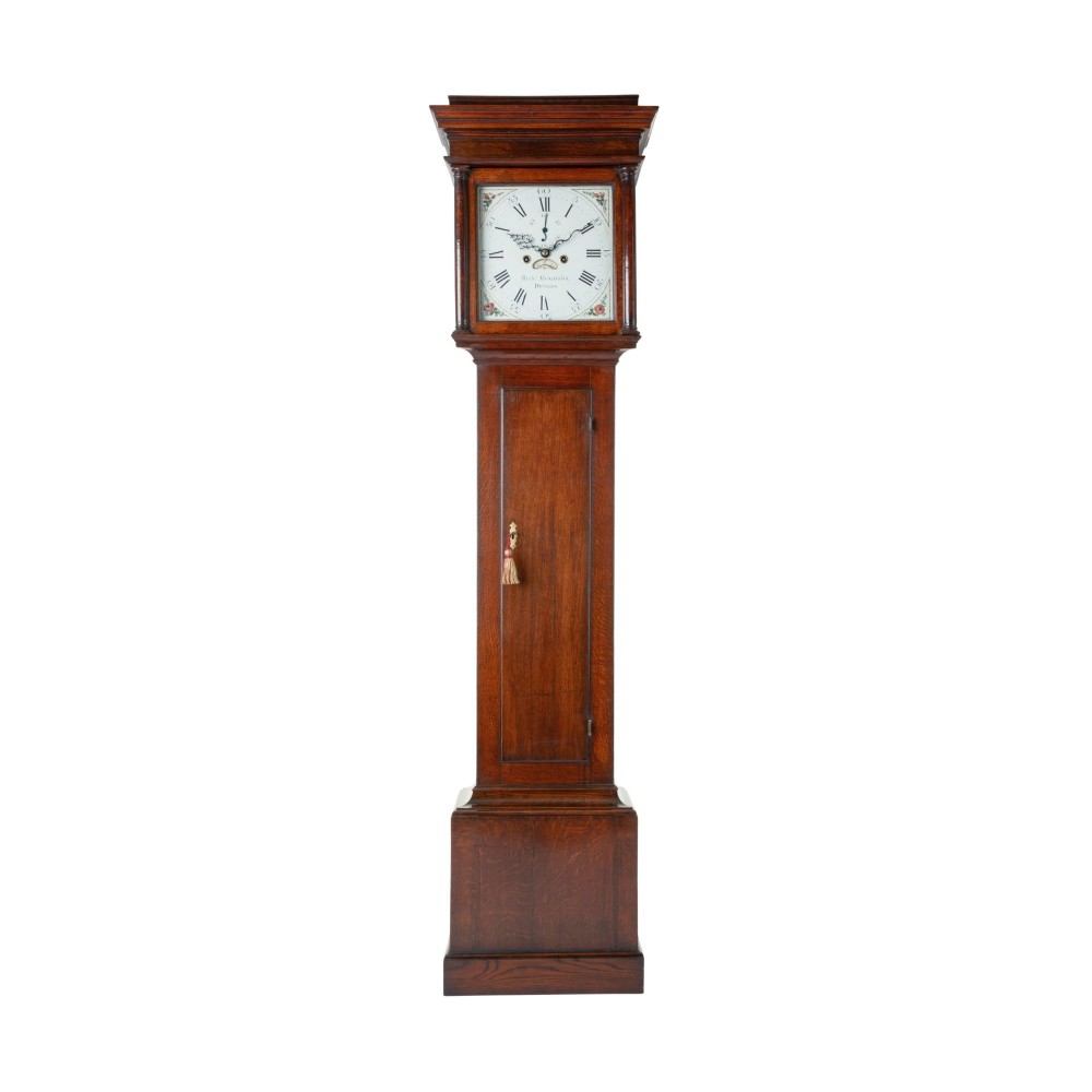 A tall Georgian oak longcase clock featuring a square painted dial, columned hood, and hinged trunk door.