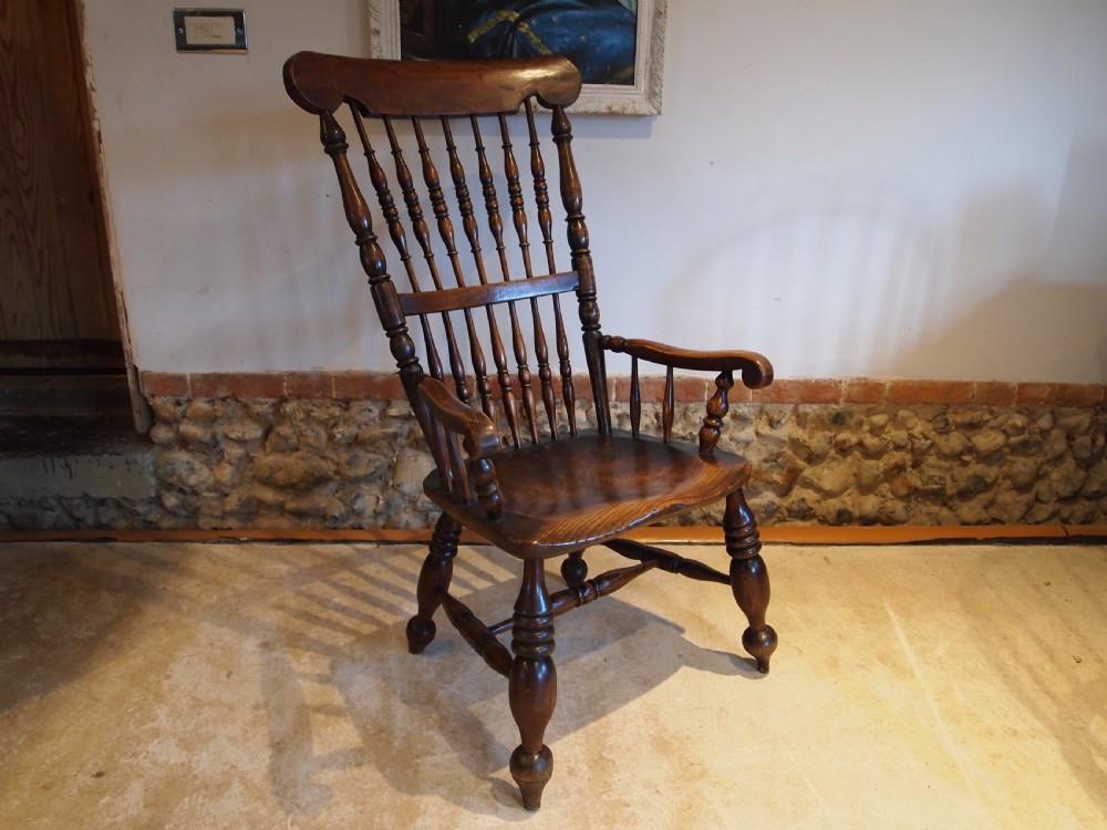 A dark brown Victorian Lincolnshire Windsor armchair featuring a turned spindle back, shaped crest rail, curved armrests, and turned legs with stretchers.
