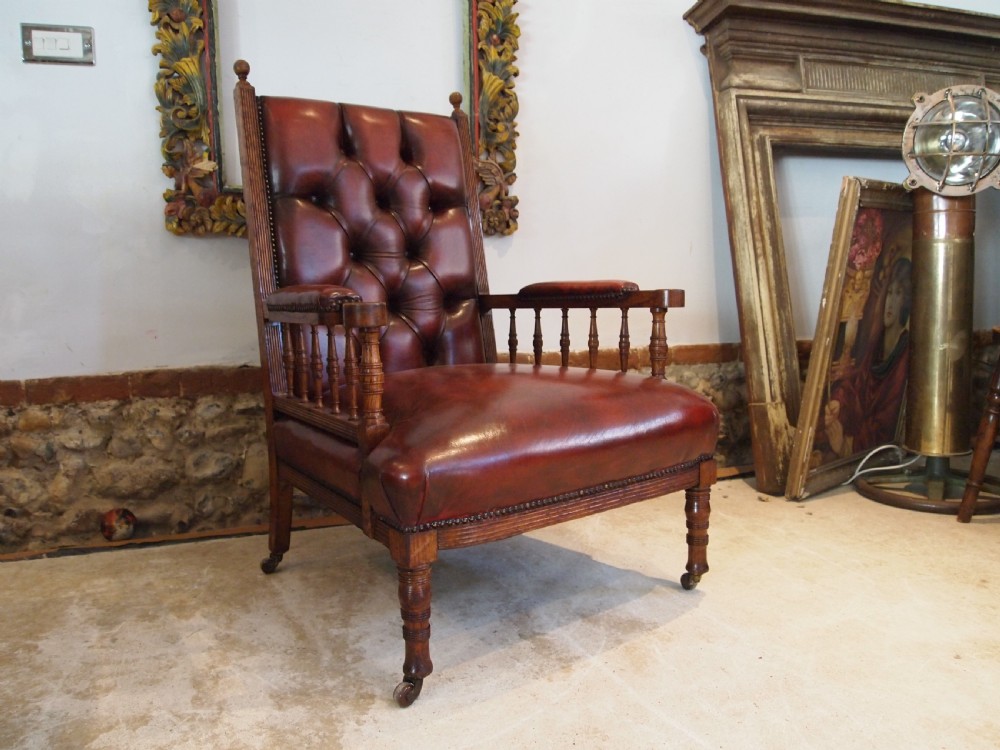 An early Victorian oak armchair with button-tufted chestnut brown leather upholstery, spindled arm supports, turned front legs, and brass casters.